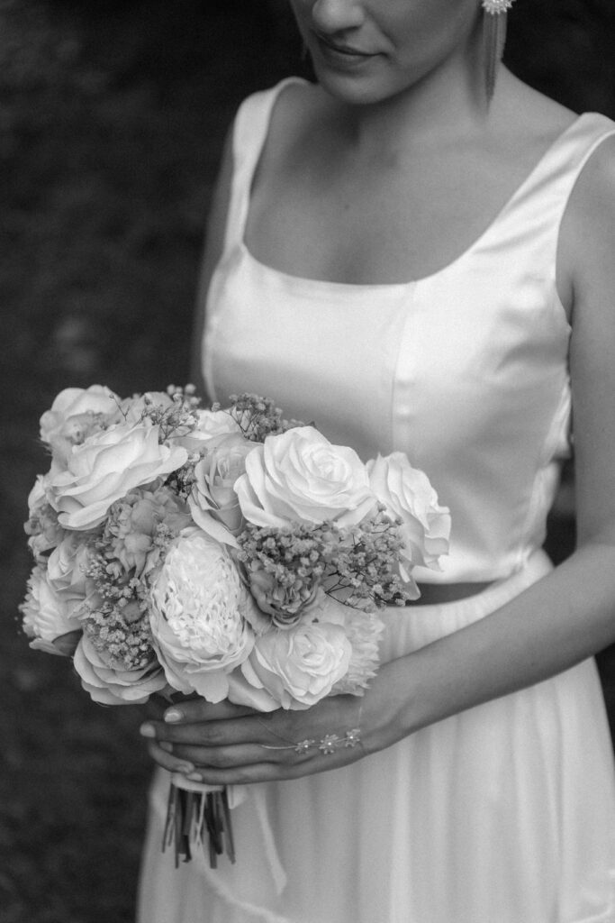 Eine Braut in einem Satinkleid aus einem Brautmodenladen in Nürnberg hält einen Strauß aus Rosen und Blumen, der von den Schultern bis zur Taille reicht.
