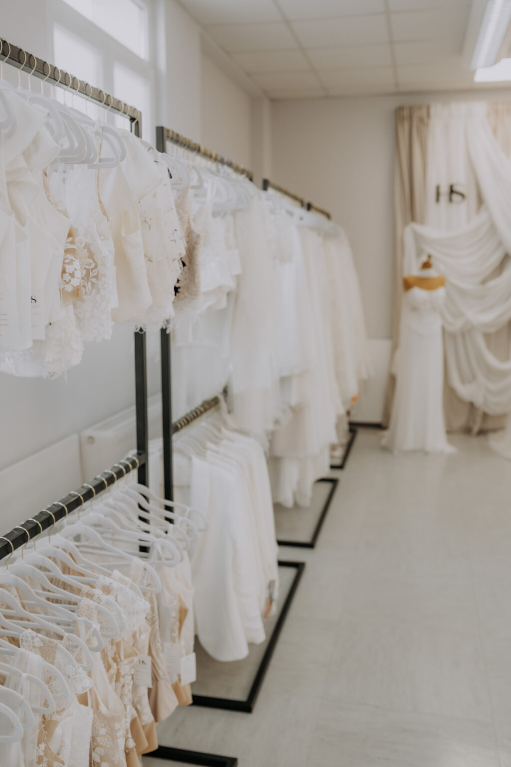 Reihen weißer Brautkleider, die in einem Brautmodengeschäft an Kleiderständern hängen, im Hintergrund eine Schaufensterpuppe.